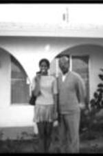Robert E. Penn and a young woman stand in front of a house. Another unidentified person stands in the doorway.