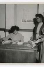 Women stand beside a desk with a sign reading "Atlanta University, Alumni Association".
