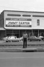 A man stands in front of downtown Plains, Georgia businesses, including a Jimmy Carter sign.