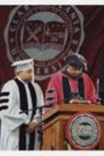 Wynton Marsalis and Thomas W. Cole, Jr., wearing graduation cap and gowns, stand at the podium at commencement.