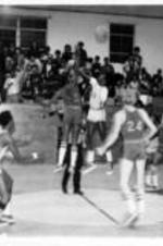 A crowd stands and looks on as two men jump in the air for the basketball.