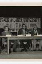 Dr. Thomas Cole sits at a table with four other men on stage in front of a sign reading: Clark Atlanta University, a Child Survival Project event.