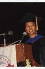 Mae Jemison, wearing a graduation cap and gown, standis at the podium at commencement.