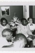 A group of men sit and listen to a speaker.