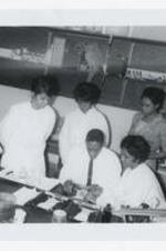 A man sits with four young women at a laboratory table with a dissected rat on a tray and other science equipment in a classroom.