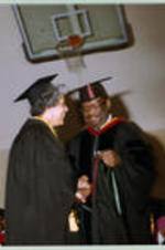 An unidentified graduate shakes James Costen's hand while she receives a red hood.