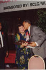 Evelyn G. Lowery is shown receiving a kiss from Harry Belafonte while Joseph E. Lowery and others watch during the 13th Annual Drum Major for Justice Awards dinner. Written on verso: 4-4-92-2 28