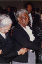 Rosa Parks is shown holding hands and bowing her head with other women at a Southern Christian Leadership Conference (SCLC) Spring Board meeting held at Grace Temple Baptist Church in Detroit, Michigan.