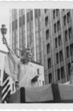 A woman dressed as the Statue of Liberty and a man dressed as Uncle Sam wave from a parade float. Written on accompanying document: Uncle Sam and Statue of Liberty.