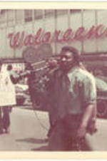 A man carries a large camera during the Sanitation Worker's Strike. Written on accompanying document: The 36 day strike of city sanitation workers demonstration, downtown Atl.