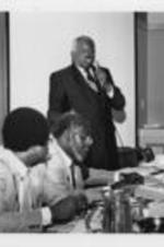 Reverend Curtis Harris is shown speaking during a Southern Christian Leadership Conference Board Luncheon as (left to right) John Nettles, N.Q. Reynolds, and S.L. Harvey listen. Written on verso: Rev. Curtis Harris, Regional Vice President reports to Board on SCLC efforts in Va. as secretary N.Q. Reynolds, Vice President John Nettles and S.L. Harvey listen.