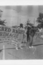 A group of demonstrators, including Southern Christian Leadership Conference leadership members (at right in the photo) are shown holding "Sacred Rights Pilgrimage" banners.