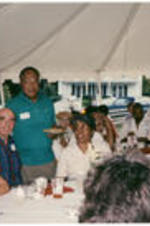 Alex Haley (standing) with a group of guests seated at tables outside of his house in Tennessee.