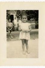 Beth I. Chandler standing in street at age 2. Written on verso: Morehouse campus age 2. Bro. Mickey in background. 5 1/2.