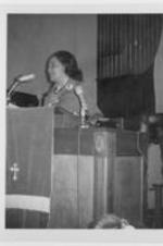 Coretta Scott King speaks at a podium in a church.