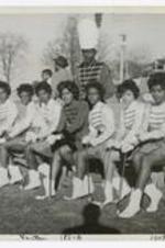 A group portrait of the majorettes seated on a bench at a football field.