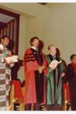 President Hugh Gloster standing on stage with Jesse Jackson and unidentified persons.