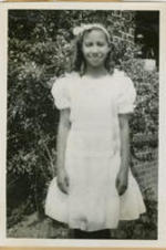 A young girl in a white dress stands outside the home.