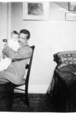 George A. Towns holds a baby inside of a home.