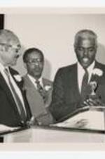 Thomas W. Cole and two men stand at the podium with a small trophy at an awards ceremony.