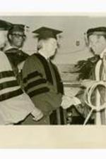 President Hugh Gloster on stage with Jimmy Carter, Dr. Willis Hubert and Dr. Abraham Davis. Written on verso: Jimmy Carter receives Morehouse Honorary Degree from Dr. Gloster, Dr. Willis Hubert, + Dr. Abraham Davis May, 1975.