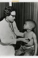View of Dr. Audrey Forbes Manley examining nephew with stethoscope. Written on verso: Dr. Audrey Forbes, C'55 examining six year old nephew Mark Simeon, ca 1962.