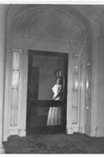 A woman in a long dress stands inside the entrance to a dormitory. Written on verso: 1946-1947