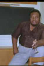 C. Eric Lincoln sits on a student desk in a classroom.