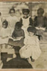 A group of children sit on steps with books. Written on recto: First family, 1903.