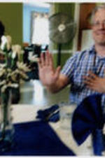 An unidentified man with glasses poses with his hand in the air.