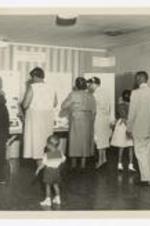 Men, women, and children examine the "Christian Education at Clark" poster display.
