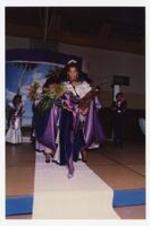 View of woman holding boquet of flowers and award trophy walking on stage. Written on verso: "Miss Morris Brown College 1987-88 Julliette Burgess".