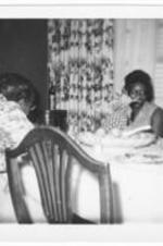 Two unidentified women sit at a dining table.
