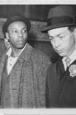 Norman Butler, the accused assassin of Malcolm X, is shown at New York City's police headquarters with a detective. Written on verso: Police hold accused Malcolm X slayer Norman 3X Butler, 26 year-old Black Muslim charged in the slaying of Black nationalist leader Malcolm X, is shown at police headquarters at 240 Centre St. in New York today after his arrest. Police called Butler an "enforcer" for the Muslims. Shown with him is a detective. 2/26/65