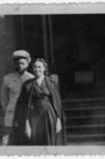 An unidentified man in military uniform stands next to an unidentified woman in front of a house.