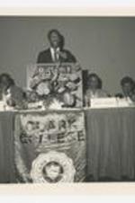 Thomas Cole stands at the podium at a Clark College banquet at the Onmi Hotel. Winifred Harris, Marey Marshall, and Maurice Pitts Page sit on either side.