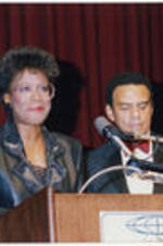 An unidentified woman stands at the podium with Andrew Young in the background at the Atlanta Student Movement 20th anniversary event.