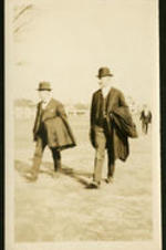 Two unidentified men walking and carrying coats.