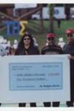 Dr. Walter Boradnax poses with two other men and a woman holding a large check "Atlanta Neurological &amp; Spine Institute, LLC, November 2, 2002, Pay to Clark Atlanta University $10,000," on football field.