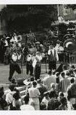 A group of young men sing and dance for a crowd in front of a building at a homecoming activity.