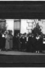 View of an unidentified group of men and women standing outside of a building.