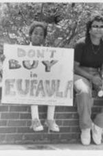 A child is shown holding a protest sign that reads "Don't Buy in Eufaula".