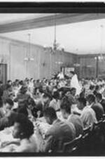 Interior of a dormitory dining hall filled with students eating at tables.