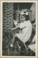 A young girl rides a tricycle with a cat on her lap.