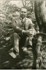 Portrait of Countee Cullen sitting on a rock. Written on verso: Photograph by Carl Van Vechten; 101 Central Park West; Cannot be reproduced without permission; June 20, 1941.