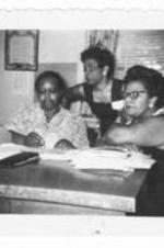 Three women sit at a desk in an office.