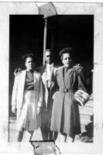 An unidentified group of a man and two women stand outside of a house.
