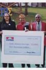 Dr. Walter Boradnax poses with another man and a woman holding a large check "Remax, October 12 2002, Pay to Clark Atlanta University $5,000," on football field.