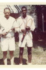 John H. Wheeler stands outside of a house with an unidentified man dressed in tennis gear, holding tennis rackets.