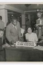 Women and men stand beside a desk with a sign reading"Atlanta University, Alumni Association".